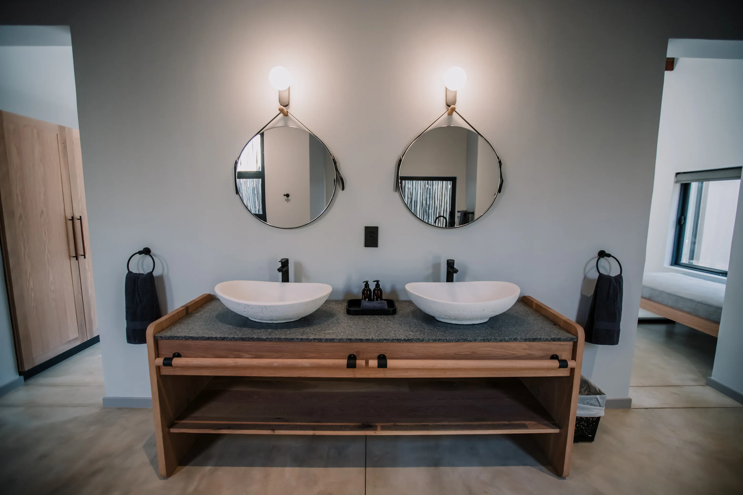 Two elegant sinks in a bathroom, each with their own circular mirror.