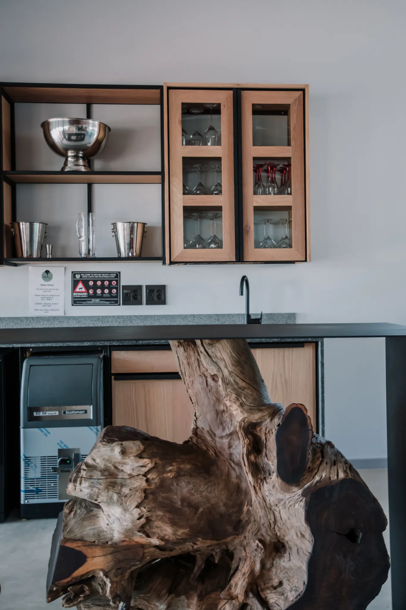 A table standing on a large tree stump in a modern kitchen with sink and built in shelves.